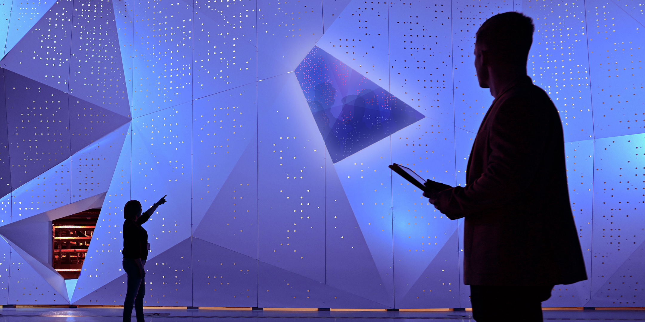 Supertietokone LUMI, jonka edessä on kaksi siluettina näkyvää ihmistä